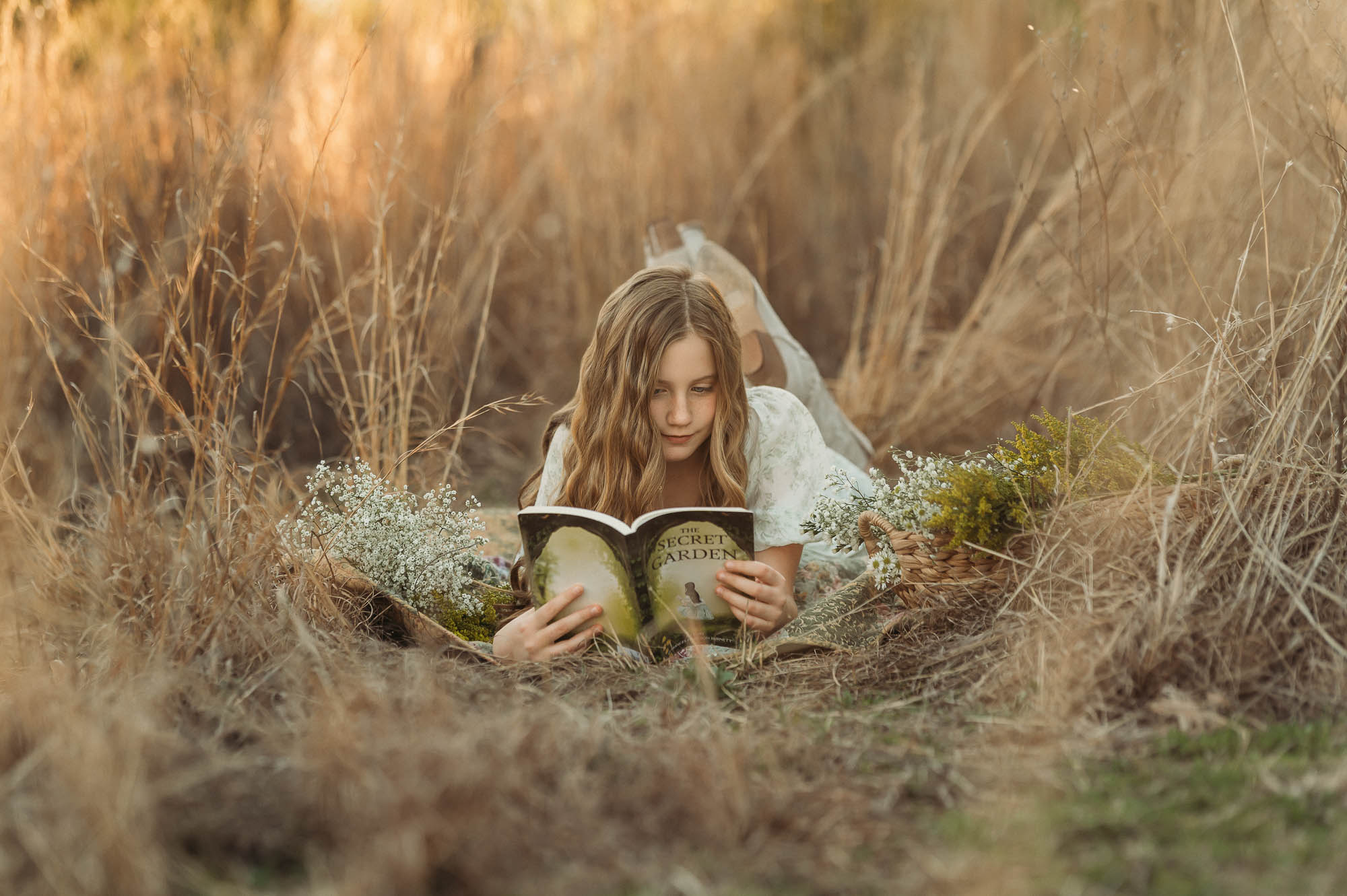 Girl reading a book surrounded by flowers and long grass | East Texas Child Photographer