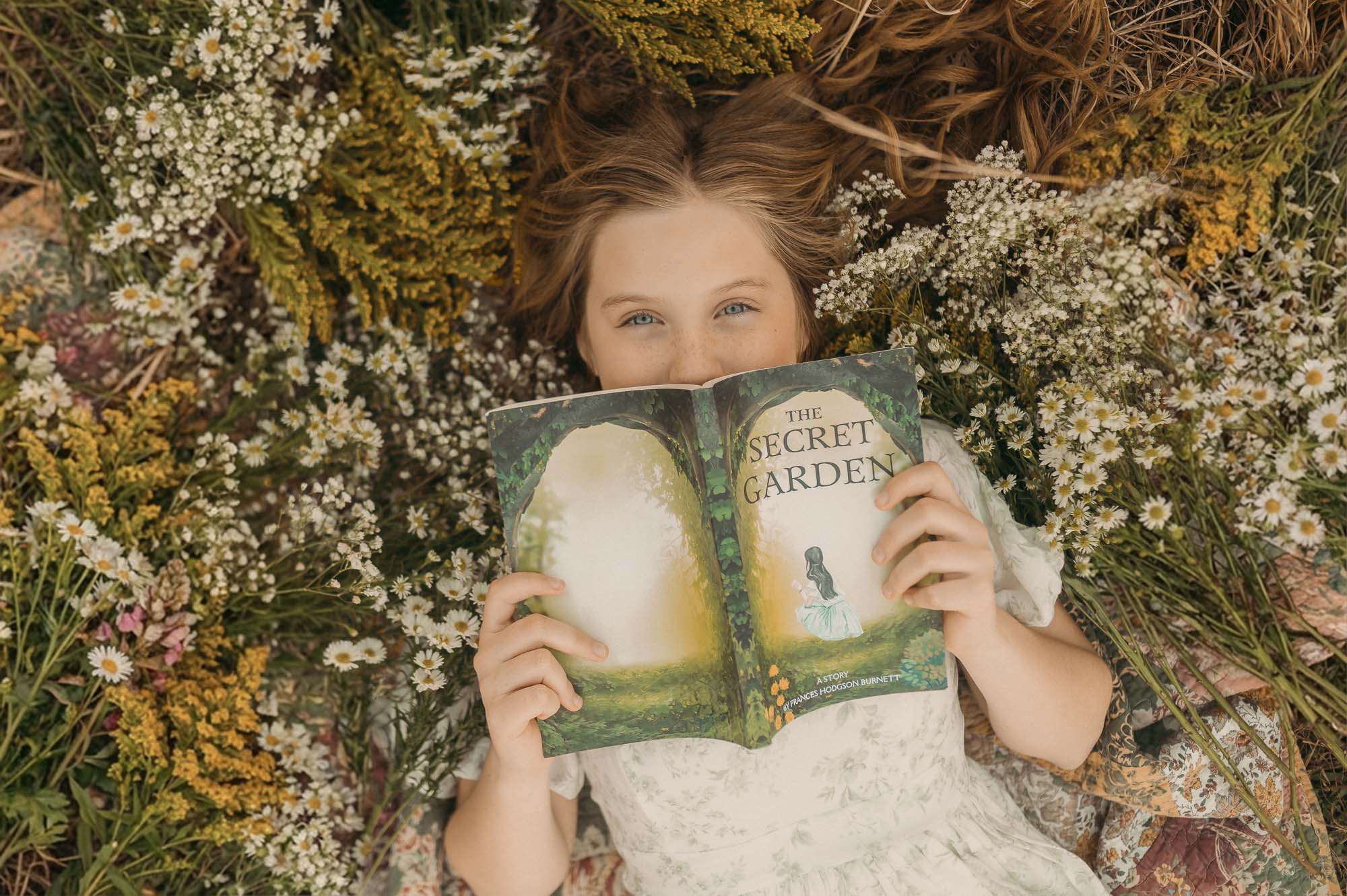 Girl reading book laying in a pile of wildflowers | East Texas Child Photographer