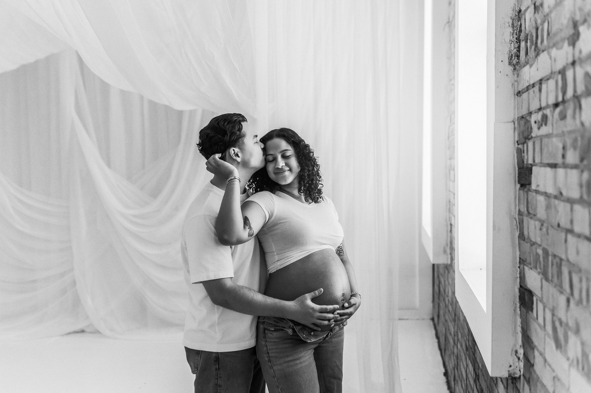 An expecting mom and dad posing in front of a studio window | Lindale Texas Maternity Photographer 