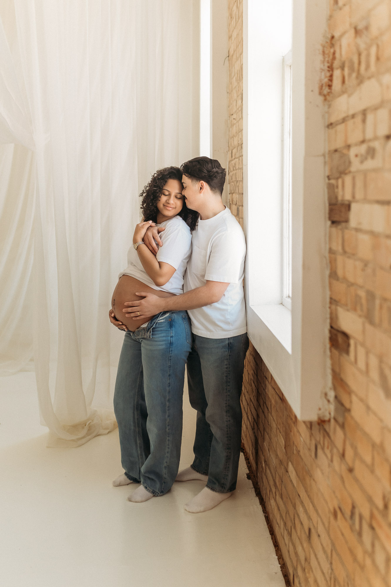 An expecting mom and dad posing in front of a studio window | Lindale Texas Maternity Photographer 