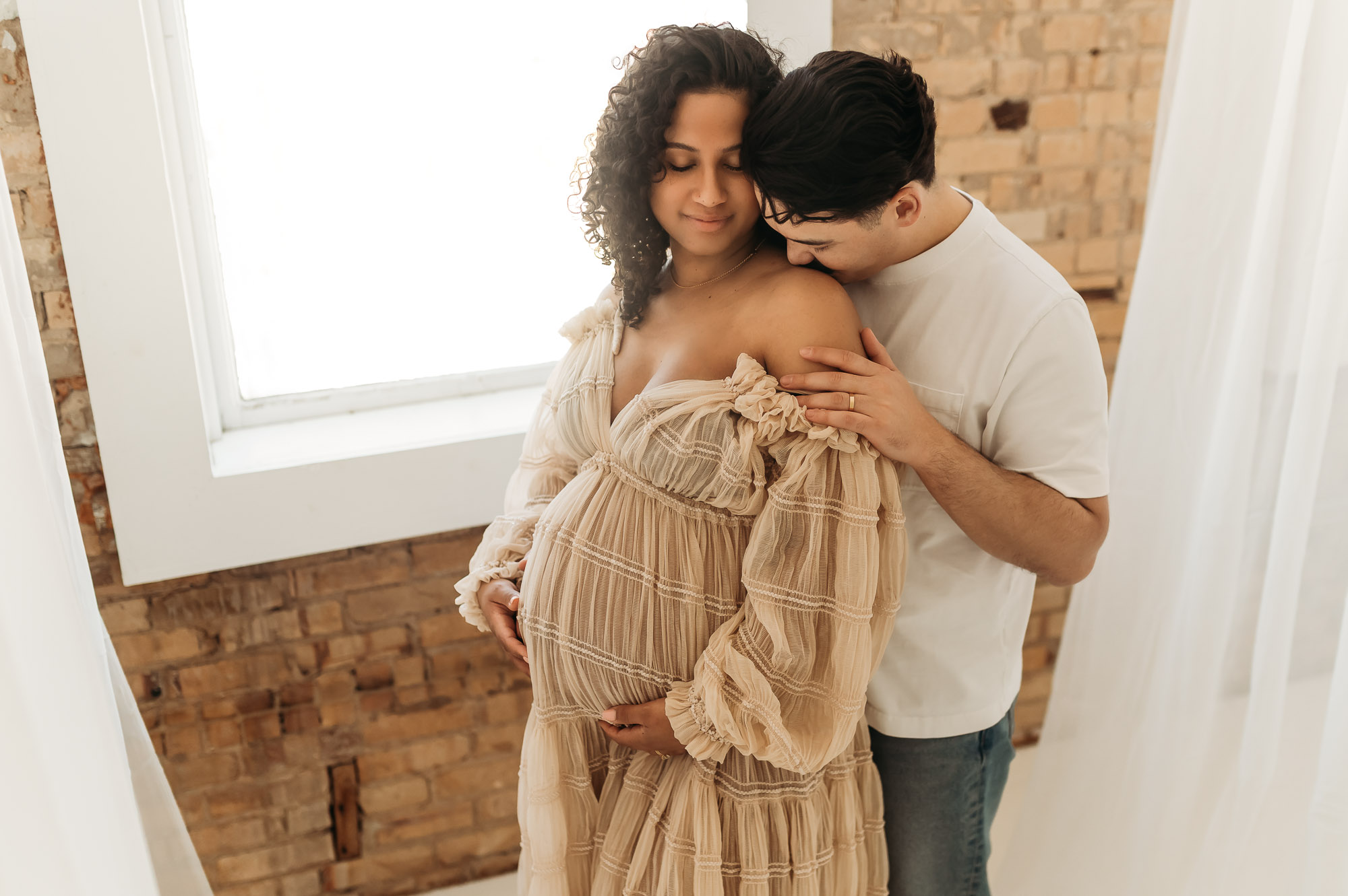 An expecting mom and dad posing in front of a studio window | Lindale Texas Maternity Photographer 
