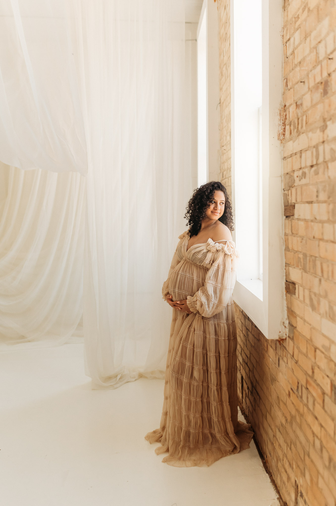 An expecting mom in a long dress posing in front of a studio window | Lindale Texas Maternity Photographer 