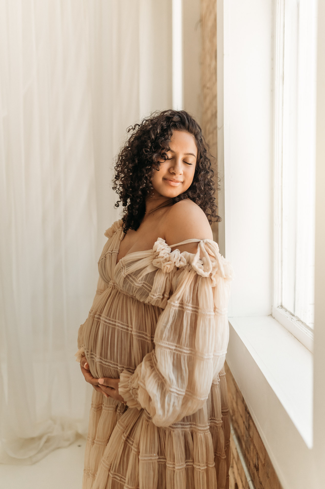 An expecting mom in a long dress posing in front of a studio window | Lindale Texas Maternity Photographer 